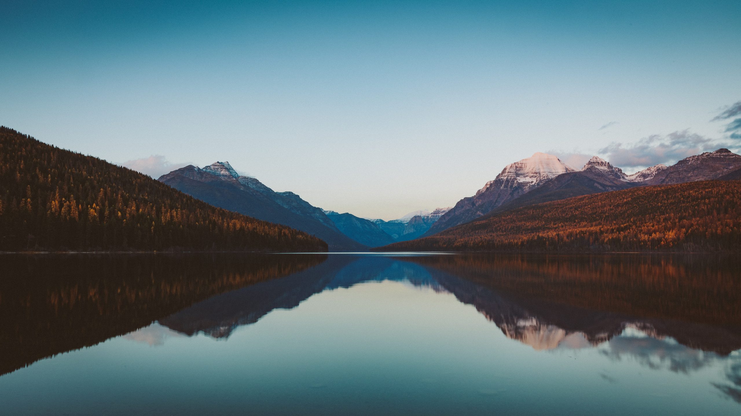 The calm waters of Bowman Lake reflect the sky and mountains on a clear fall evening.